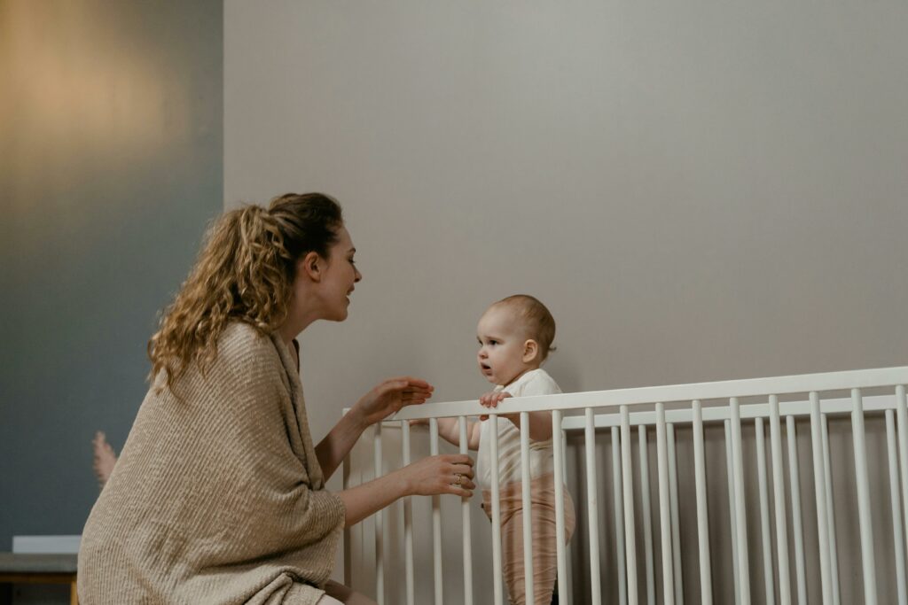 Postpartum Doulas Sleep Train - woman sits next to crib while infant stands in crib
